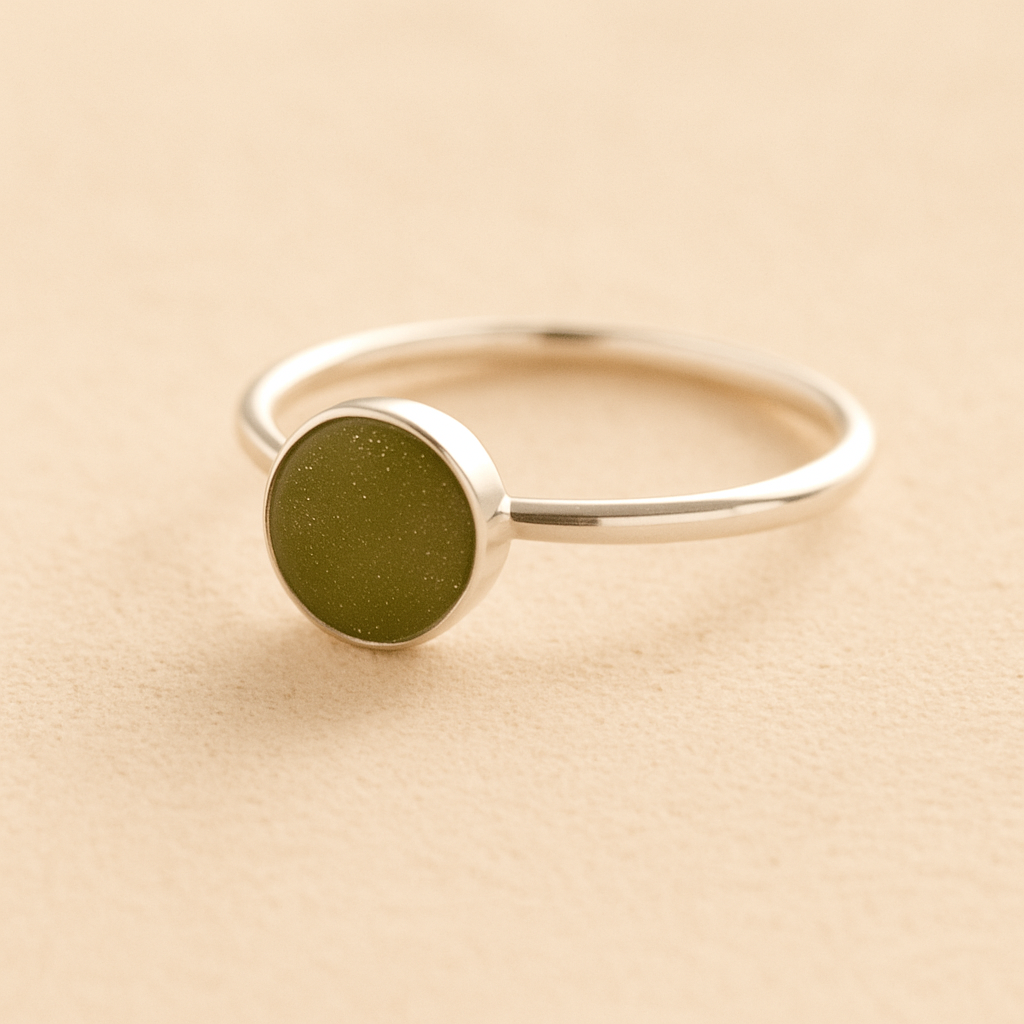 Silver cremation ashes ring with a sage resin circle bezel filled with ashes or fur on a beige background