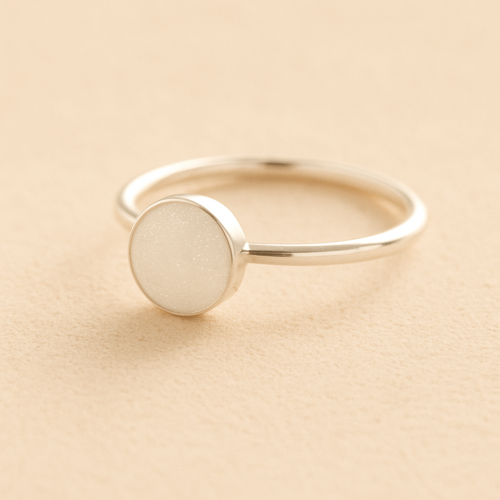 Silver cremation ashes ring with a white resin circle bezel filled with ashes or fur on a beige background