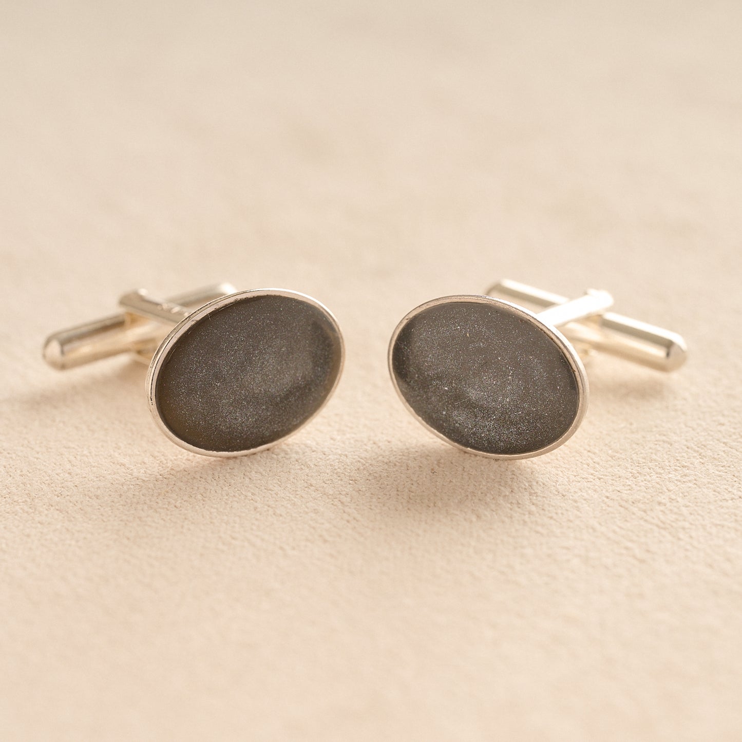 Silver oval memorial cufflinks with a grey resin infill made with ashes or fur on a beige background