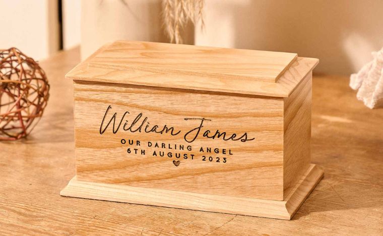 Wooden infant urn with engraved text on a wooden surface