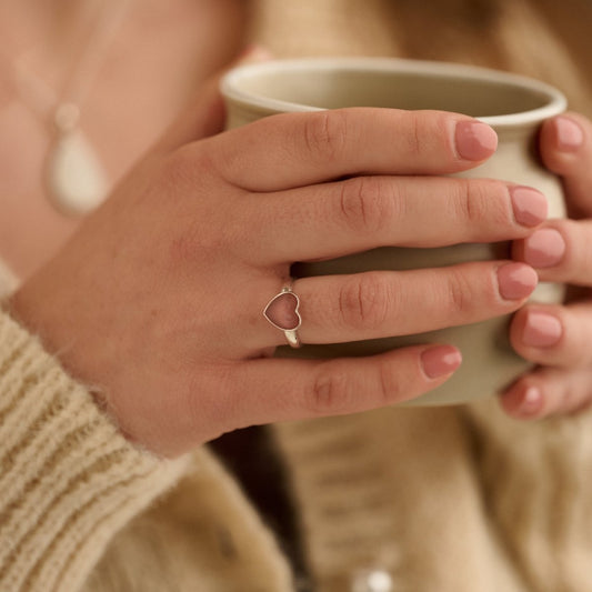 Woman wearing dark pink sterling silver cremation ring while holding a cup of tea in a reflective moment.