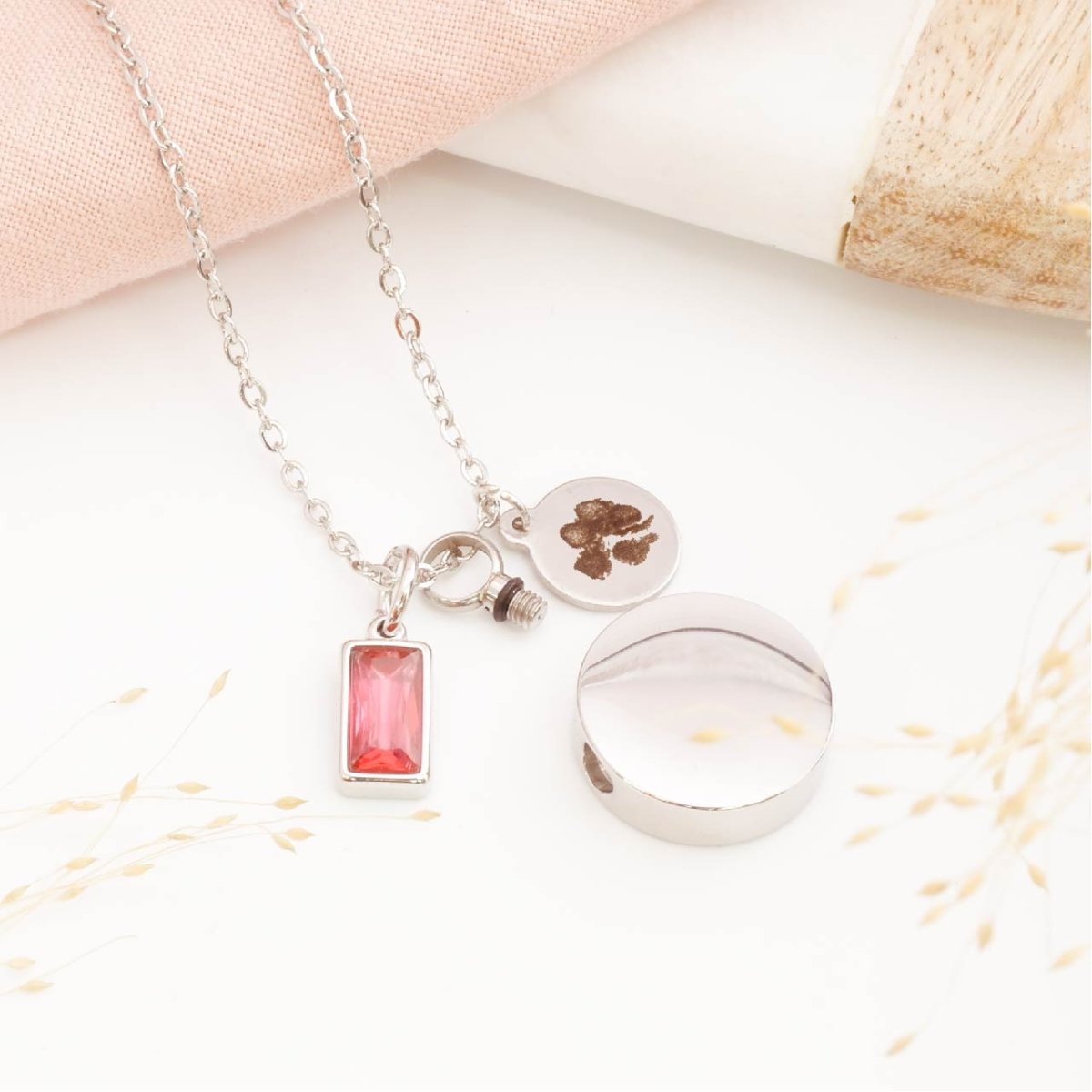 Paw print necklace with self fill urn pendant and birthstone charm on a light background. Memorial Jewellery for him