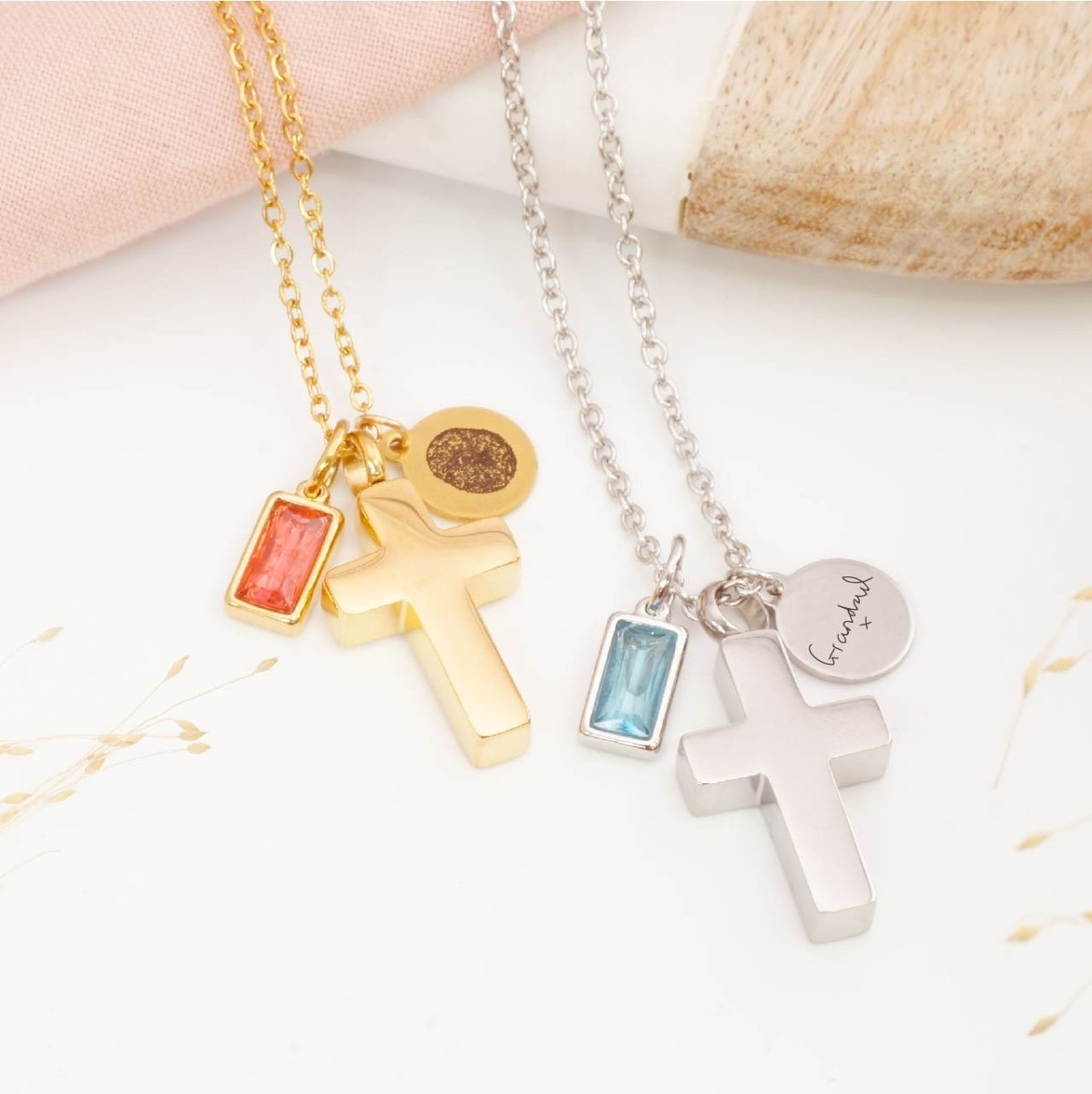 Two cross-shaped urn necklaces, with fingerprint engraving and handwriting engraving one gold and one silver, on a light background.