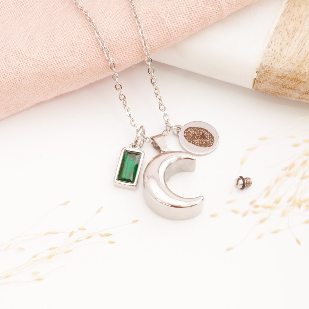 A personalised moon cremation necklace with fingerprint engraving on a table