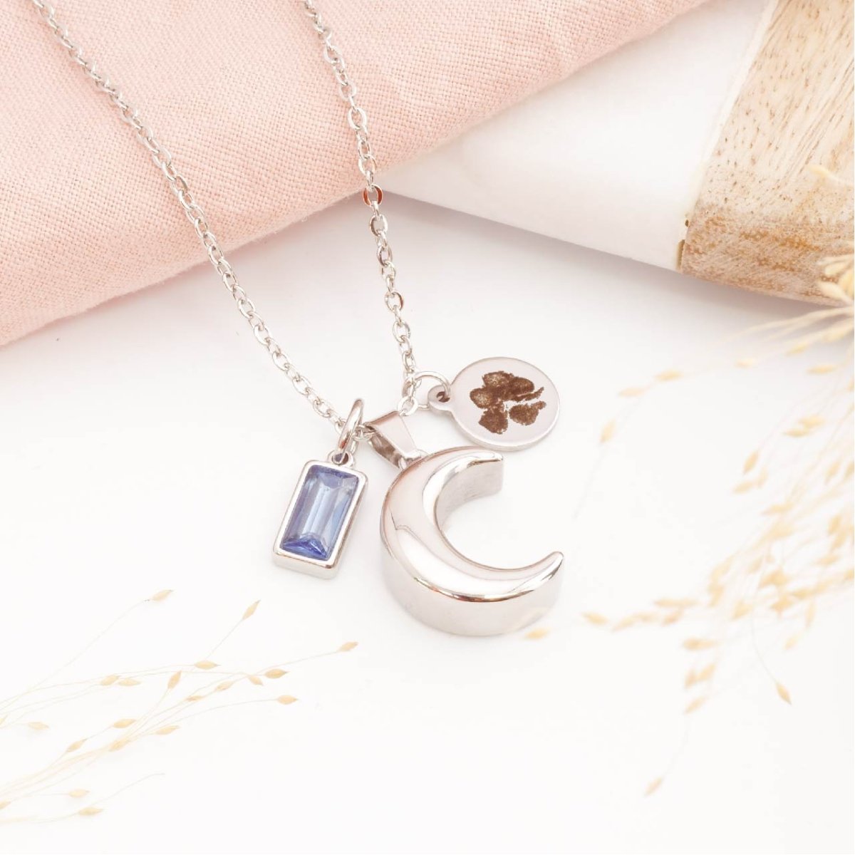 Self fill moon cremation necklace with pawprint engraving on a table