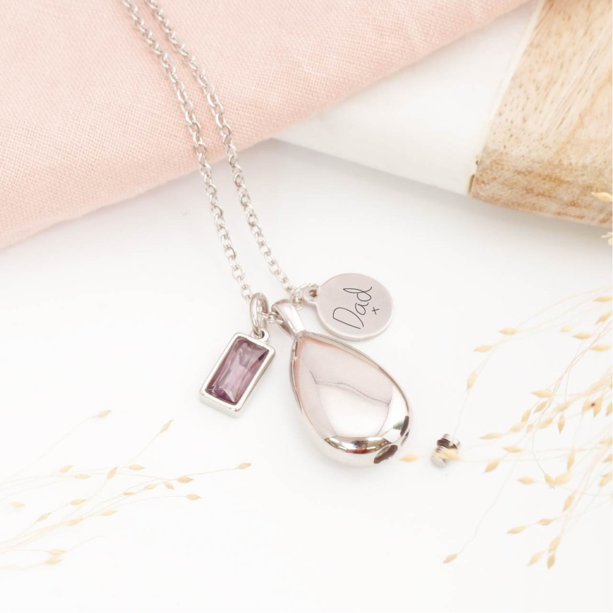Handwriting jewellery, with teardrop shape memorial pendant and birthstone charm on a light background. Memorial necklaces UK