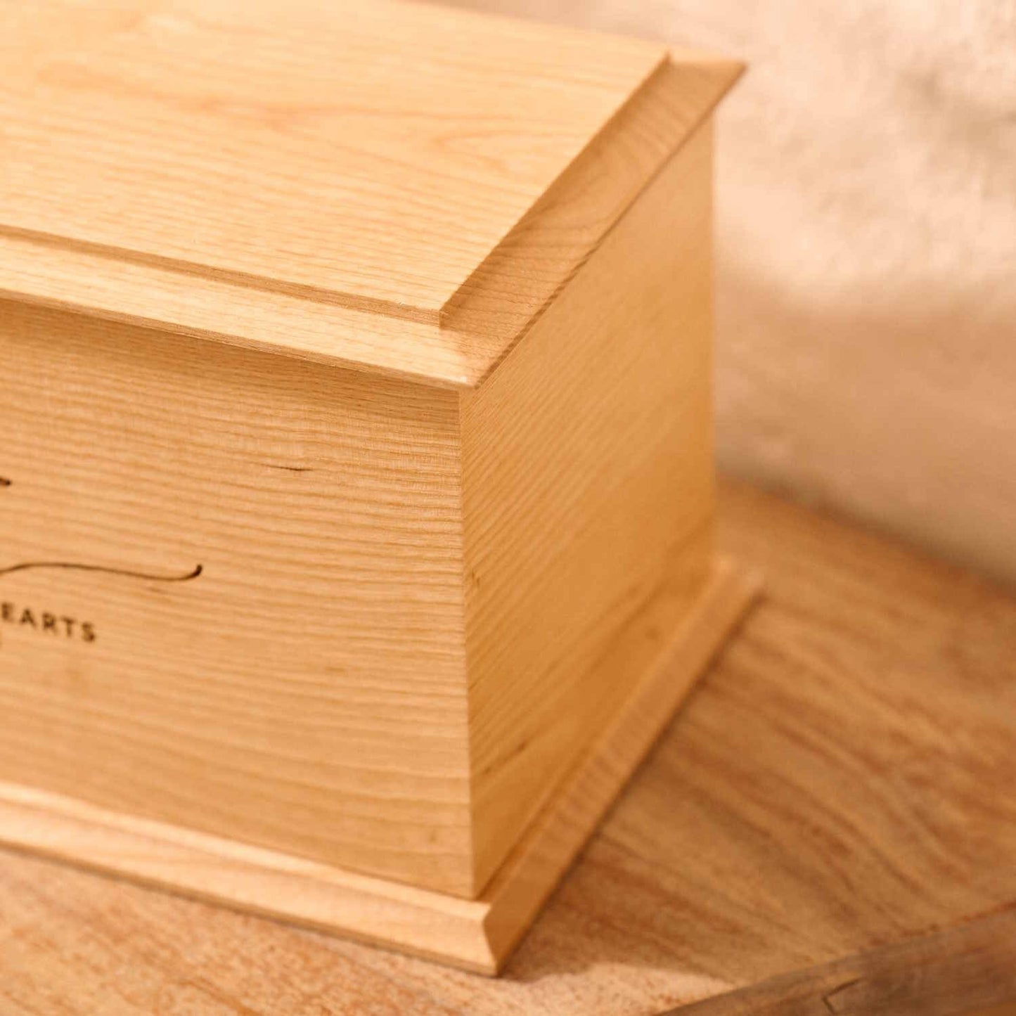 Close-up of engraved ash wood cremation urn with laurel wreath design – detailed view of custom memorial