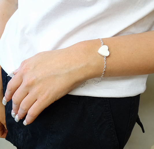 Person wearing a silver bracelet with a heart-shaped charm on a plain background