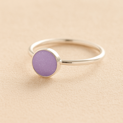 Silver memorial ashes ring with a lavender resin circle bezel on a beige background