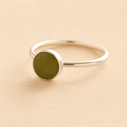 Silver cremation ashes ring with a sage resin circle bezel filled with ashes or fur on a beige background