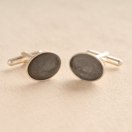 Silver oval memorial cufflinks with a grey resin infill made with ashes or fur on a beige background
