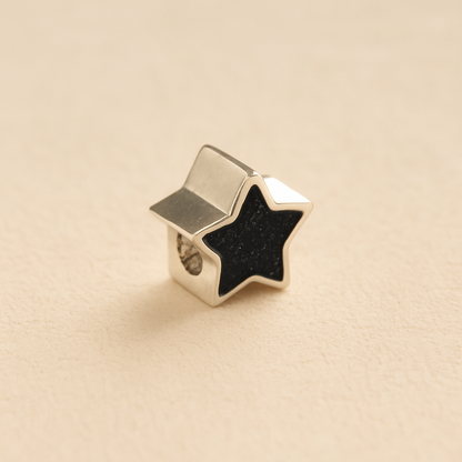 Silver star-shaped Memorial Charm Bead with black resin on a beige background