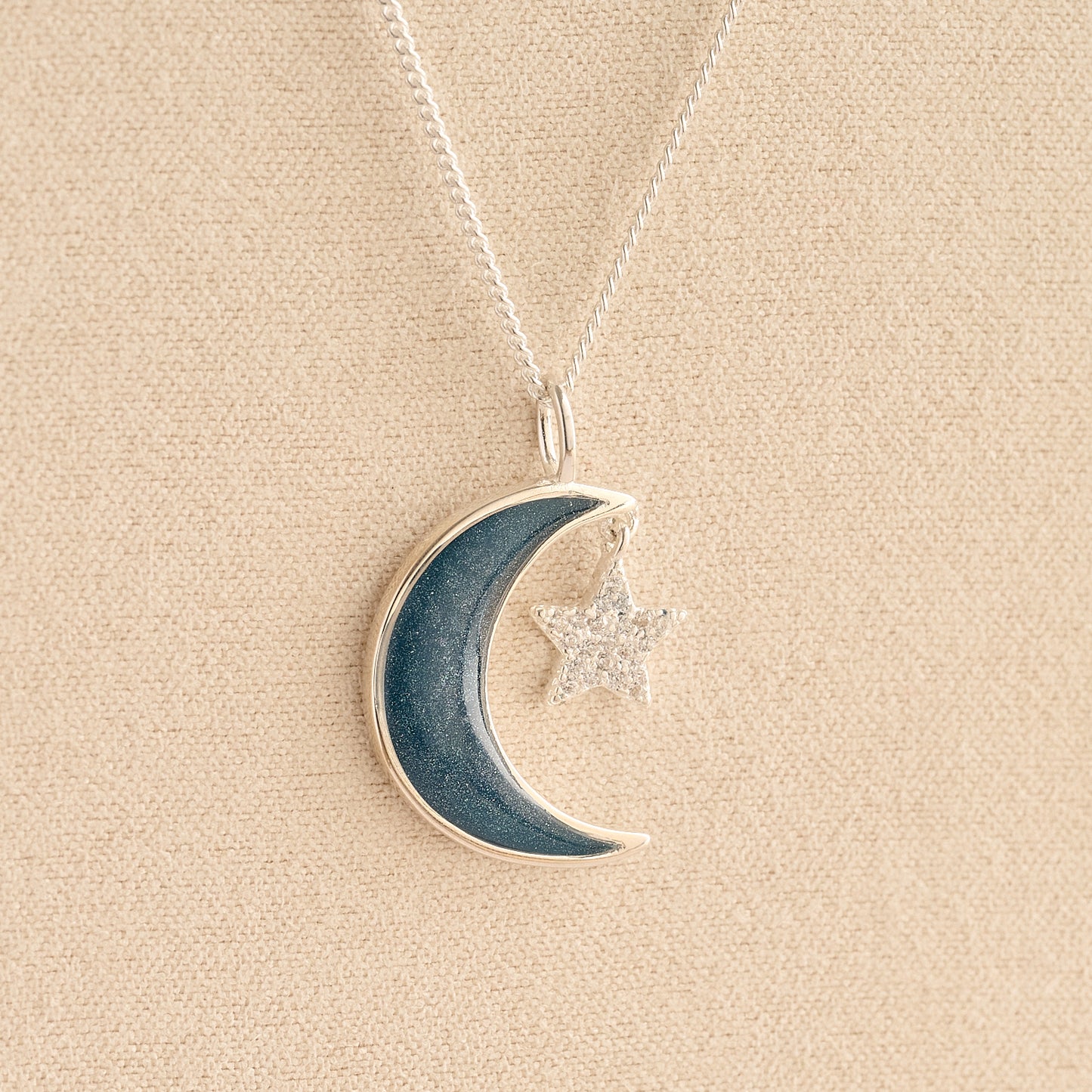 Moon and Star Ashes Necklace with navy resin filled with ashes or fur on a beige textured background