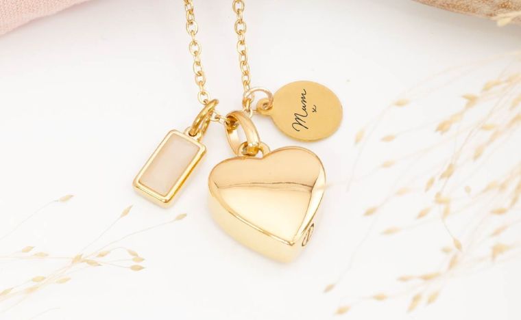 Gold heart-shaped urn necklace with engraved tag on a light background