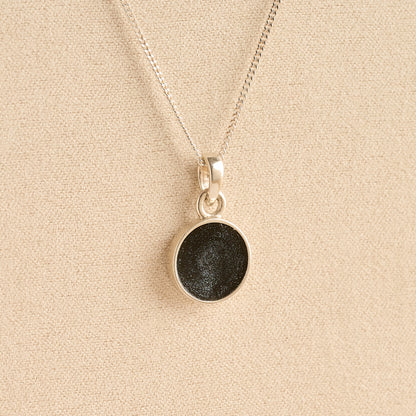 Silver Cremation ashes necklace with a round pendant and black resin filled with ashes or fur, displayed on a soft beige background – suitable for pet or human memorials.