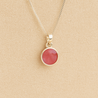 Silver Cremation ashes necklace with a round pendant and dark pink resin filled with ashes or fur, displayed on a soft beige background – suitable for pet or human memorials.