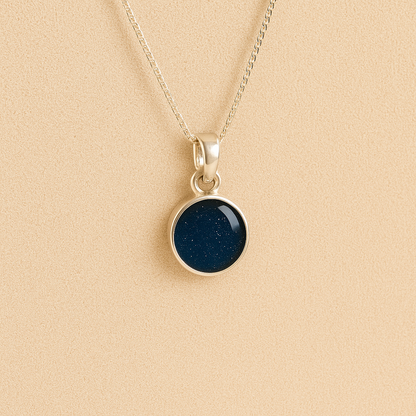 A round Silver Cremation ashes necklace navy resin filled with ashes or fur, displayed on a soft beige background – suitable for pet or human memorials.