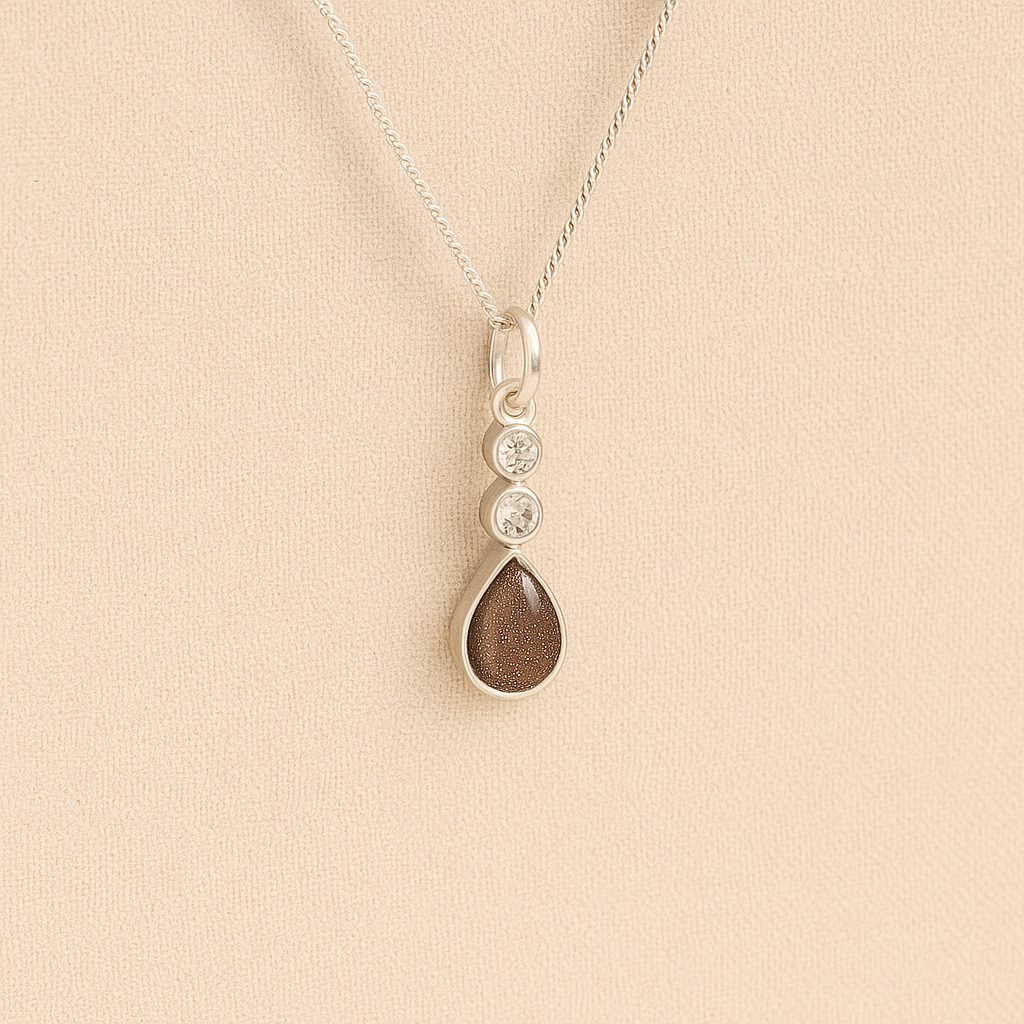 Silver Cremation ashes necklace with a teardrop pendant and mocha resin filled with ashes or fur, displayed on a soft beige background – suitable for pet or human memorials.