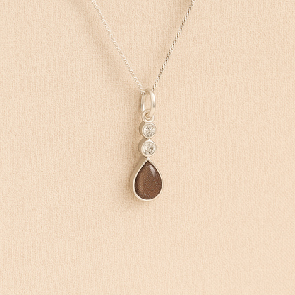 Silver Cremation ashes necklace with a teardrop pendant and mocha resin filled with ashes or fur, displayed on a soft beige background – suitable for pet or human memorials.