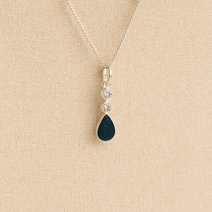Silver Cremation ashes necklace with a teardrop pendant and navy resin filled with ashes or fur, displayed on a soft beige background – suitable for pet or human memorials.