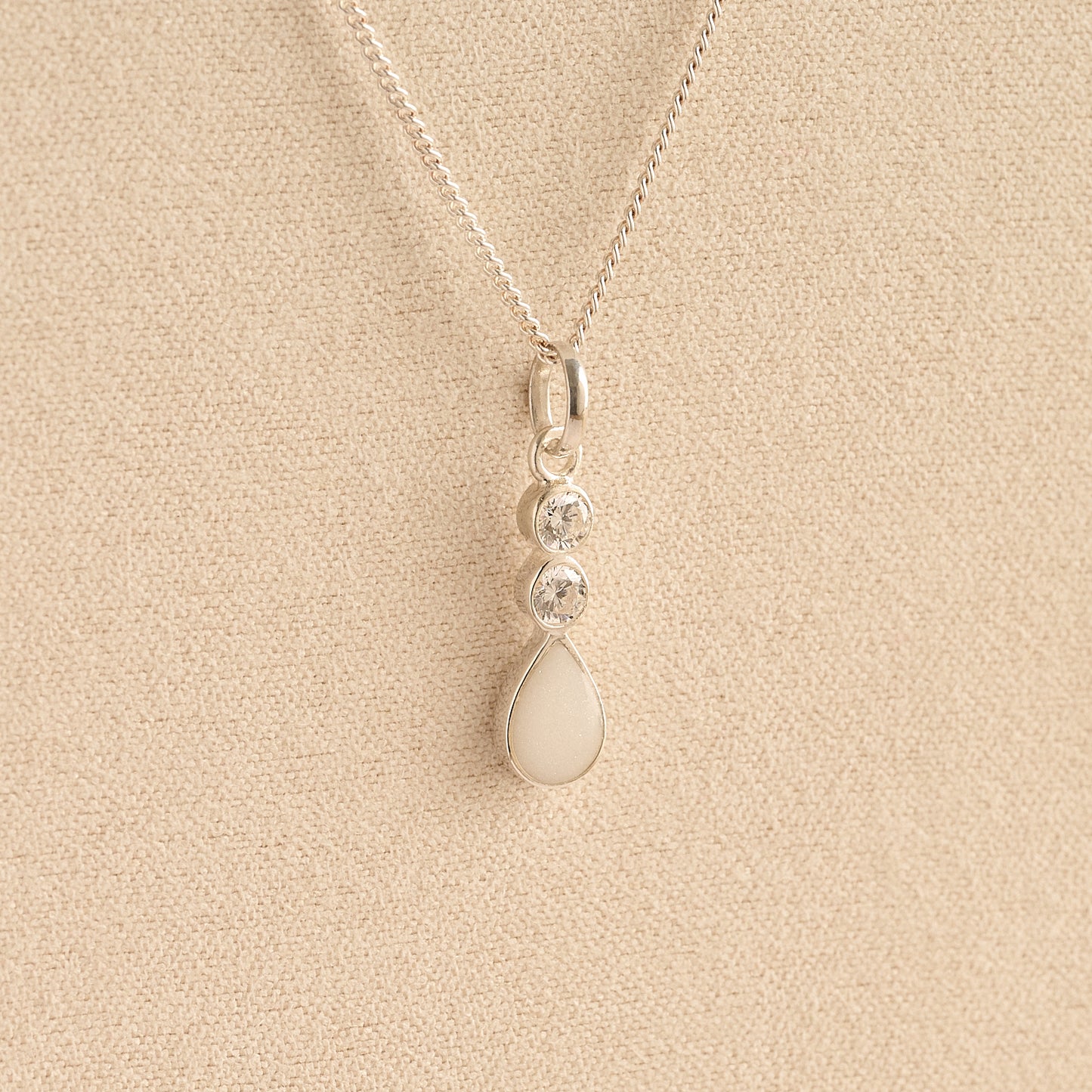 Silver Cremation ashes necklace with a teardrop pendant and white resin filled with ashes or fur, displayed on a soft beige background – suitable for pet or human memorials.