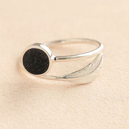 Silver adjustable feather ashes ring with a black resin on a beige background