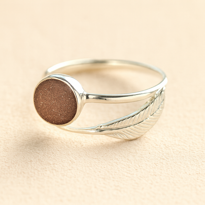 Adjustable Silver feather ashes ring with a mocha resin on a beige background