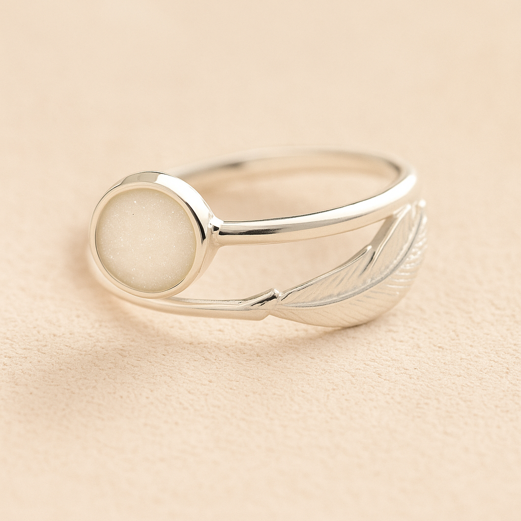 Silver adjustable feather ring with ashes and a white resin on a beige background