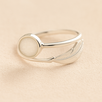 Silver adjustable feather ring with ashes and a white resin on a beige background