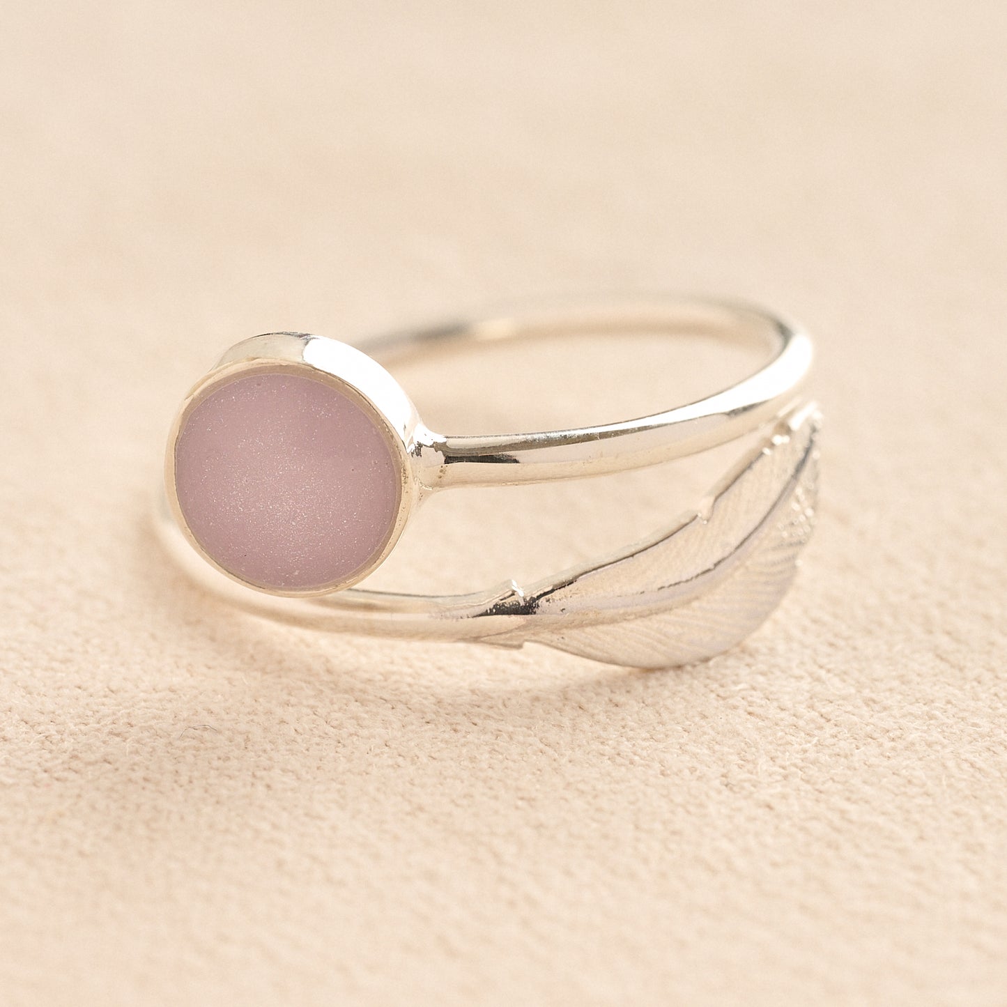 Adjustable Silver ashes ring with a lavender resin and feather on a beige background