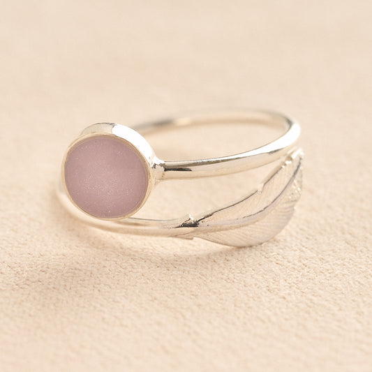 Adjustable Silver ashes ring with a lavender resin and feather on a beige background