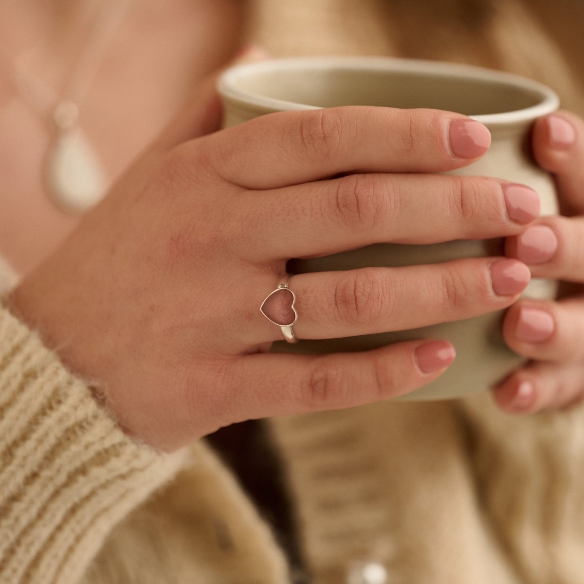 Woman wearing dark pink sterling silver cremation ring while holding a cup of tea in a reflective moment.