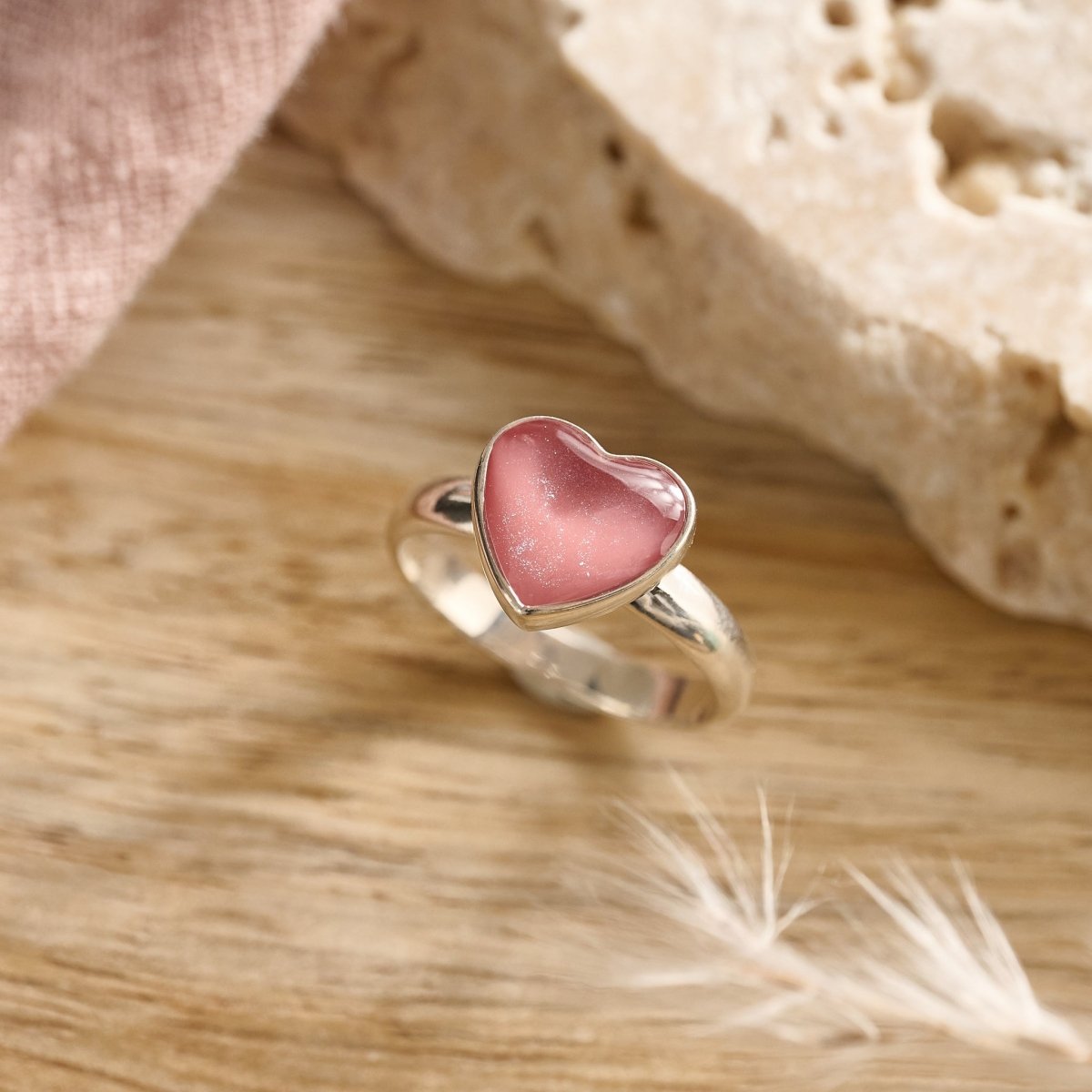 Dark pink resin cremation ashes ring in sterling silver displayed on wood