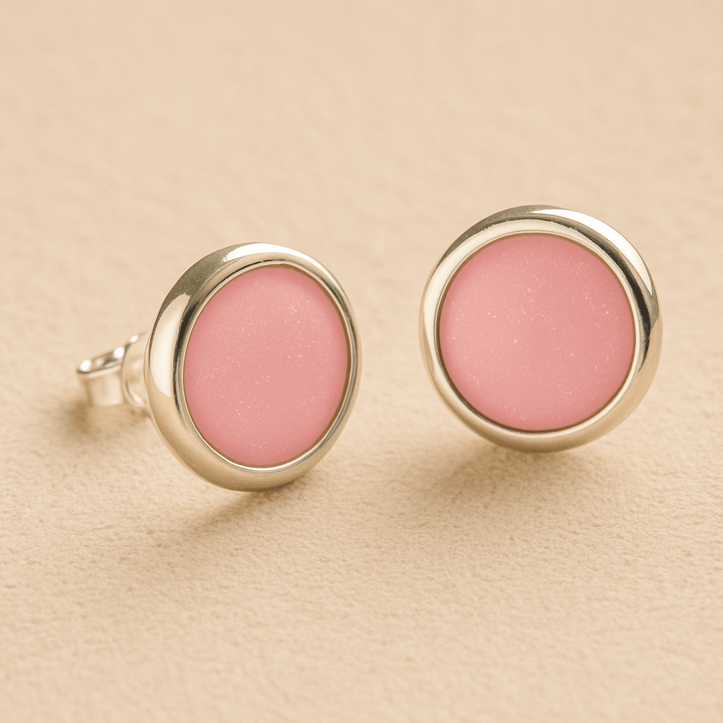 A pair silver round memorial earrings with light pink resin in made from ashes, fur or hair set on a beige background