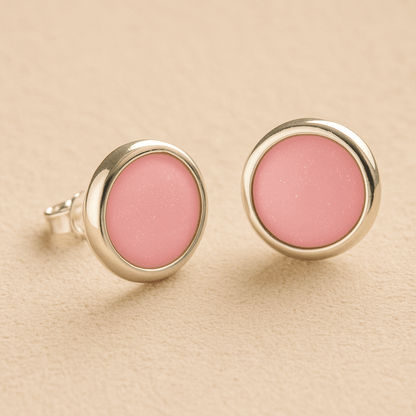 A pair silver round memorial earrings with light pink resin in made from ashes, fur or hair set on a beige background