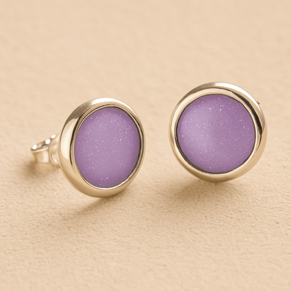 A pair silver round memorial earrings with lavender resin in made from ashes, fur or hair set on a beige background