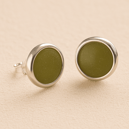 A pair silver round ashes earrings with sage resin in made from ashes, fur or hair set on a beige background