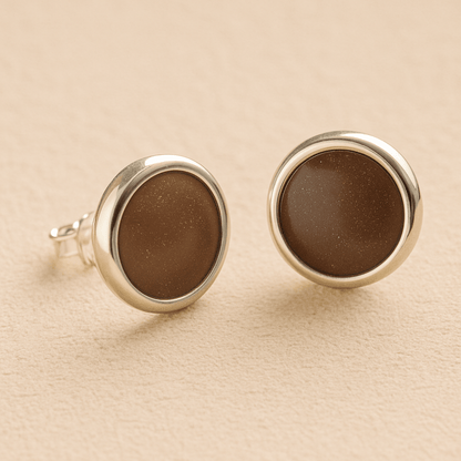 A pair silver round memorial earrings with mocha resin in made from ashes, fur or hair set on a beige background