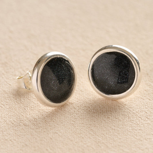 A pair silver round ashes earrings with black resin in made from ashes, fur or hair set on a beige background