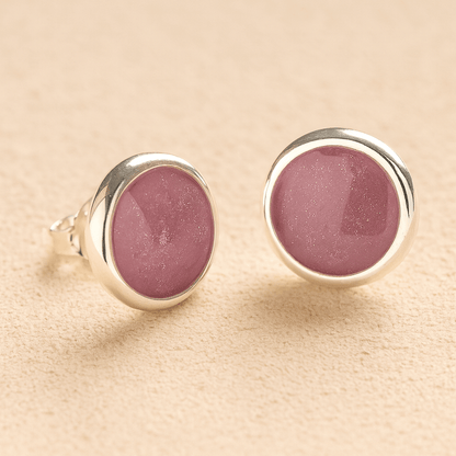 A pair silver round ashes earrings with dark pink resin in made from ashes, fur or hair set on a beige background