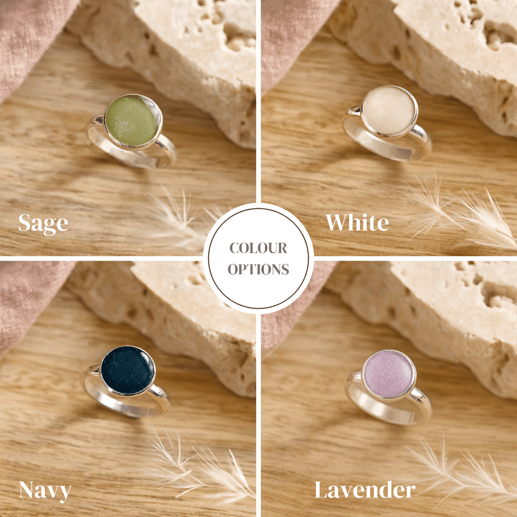 Four silver cremation rings with different colored gemstones on a wooden surface.