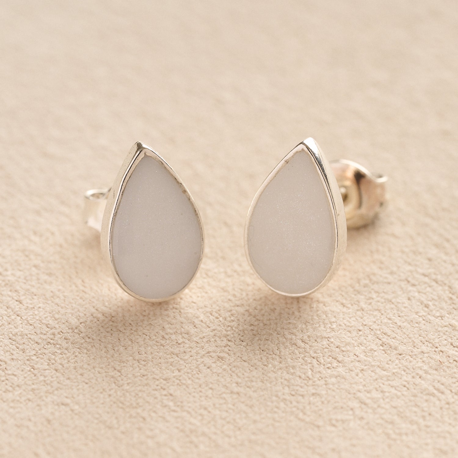 Memorial Ashes Teardrop Stud Earrings with white resin on a beige fabric background