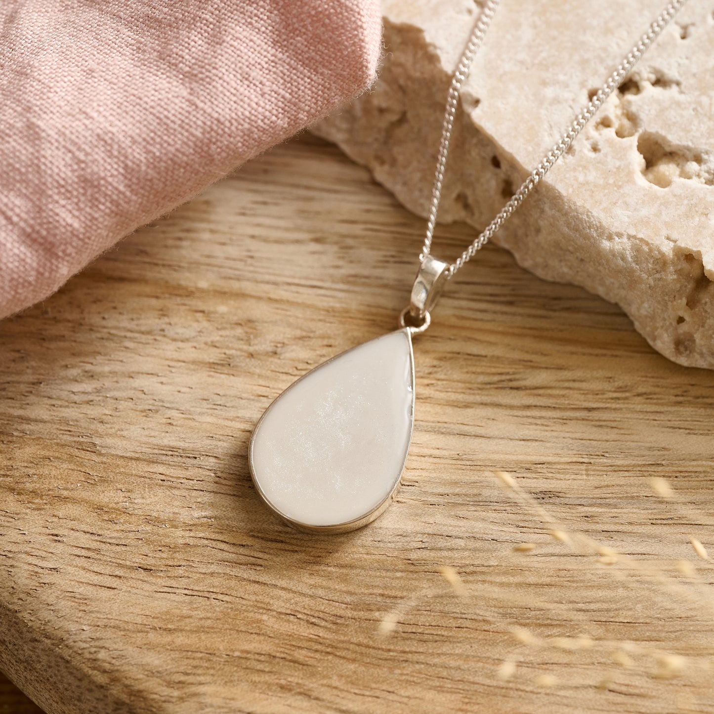 Teardrop-shaped cremation ashes necklace in soft white resin resting on a wooden table