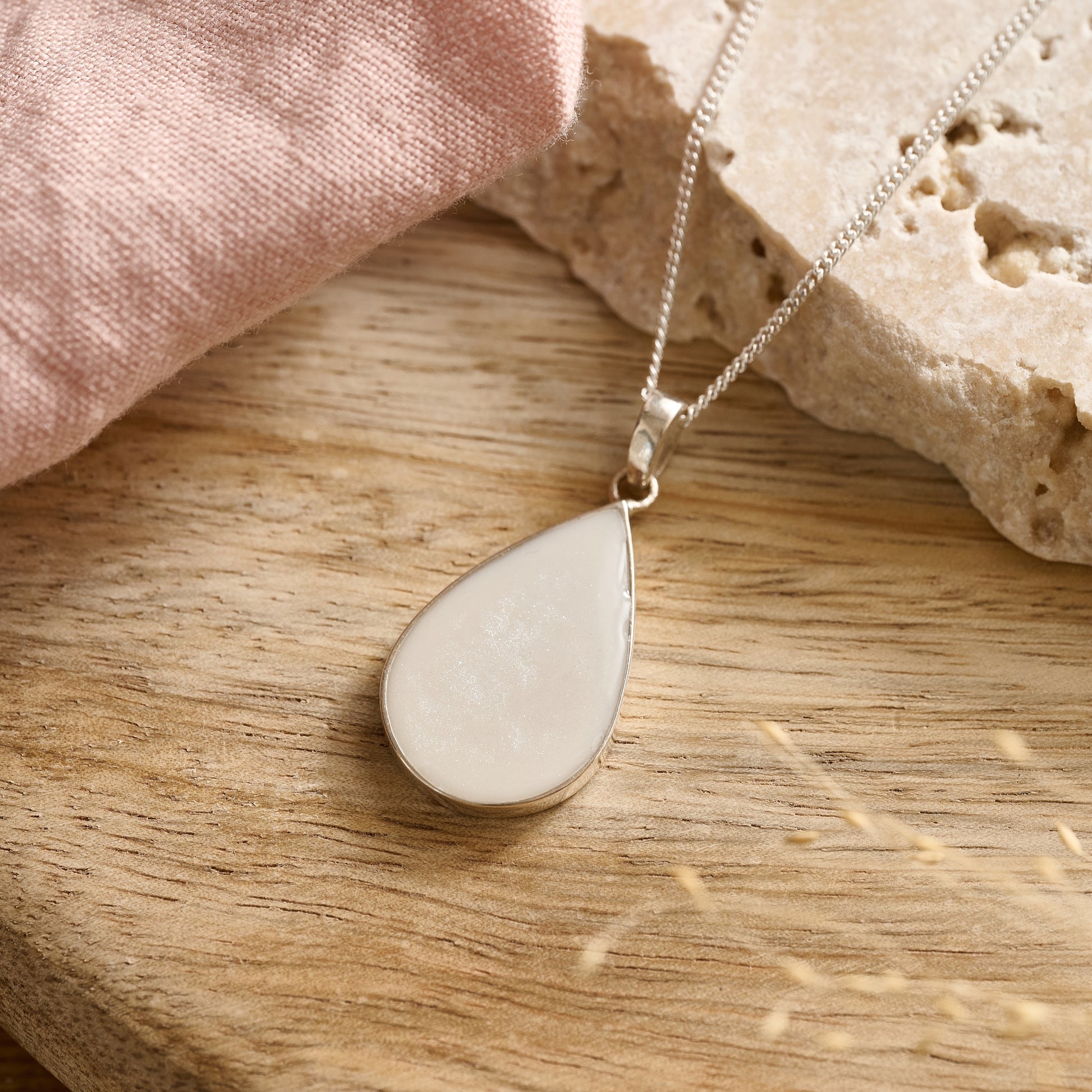 Teardrop-shaped cremation ashes necklace in soft white resin resting on a wooden table