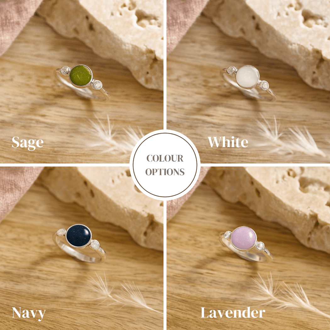 Four silver cremation rings with different colored gemstones on a wooden surface.