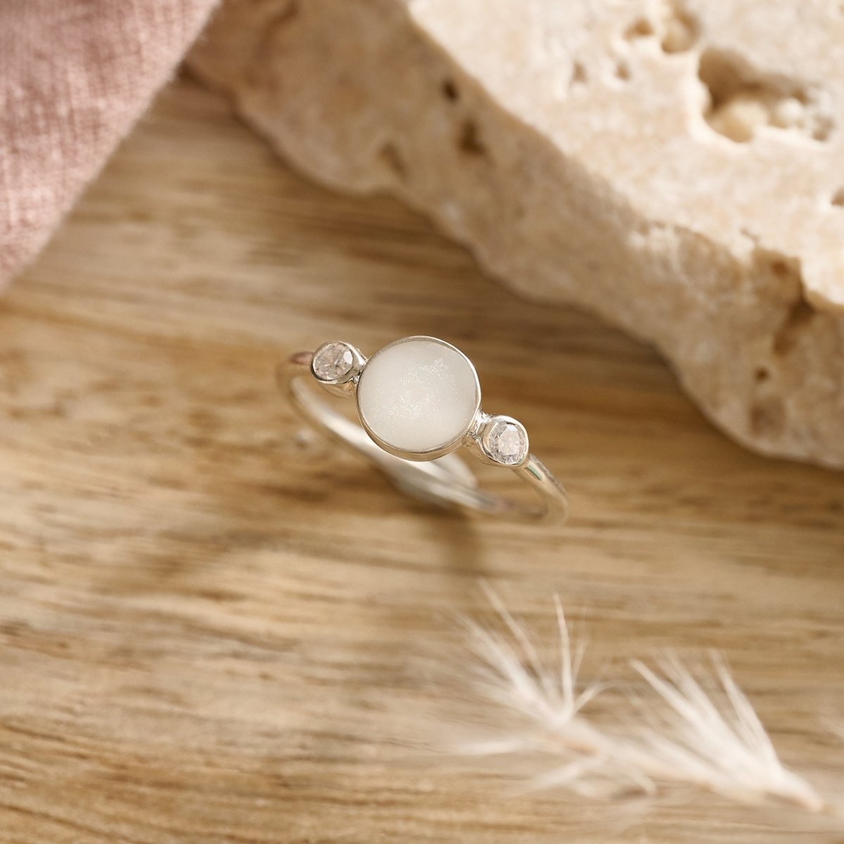 Flatlay of sterling silver cremation ring with crystals and white resin on wood
