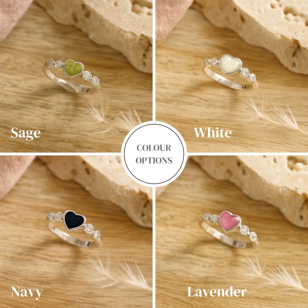 Four silver cremation rings with different gemstones on a wooden surface, labeled Sage, White, Navy, and Lavender.
