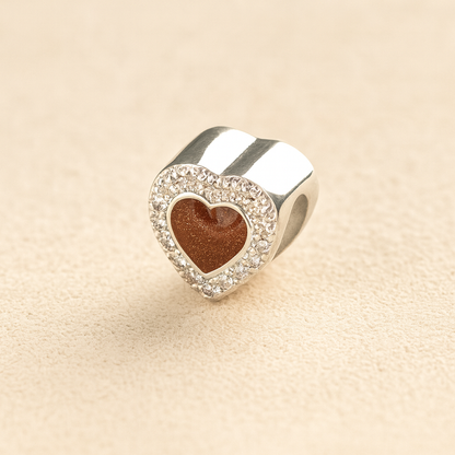 Silver heart-shaped Pandora cremation charm with a mocha resin center on a beige background