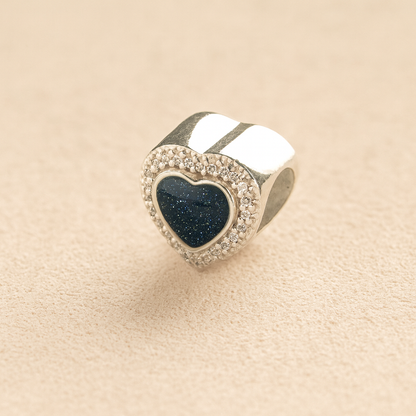 Sterling Silver Heart-shaped ashes charm with a navy resin infill and CZ crystals surround on a beige background