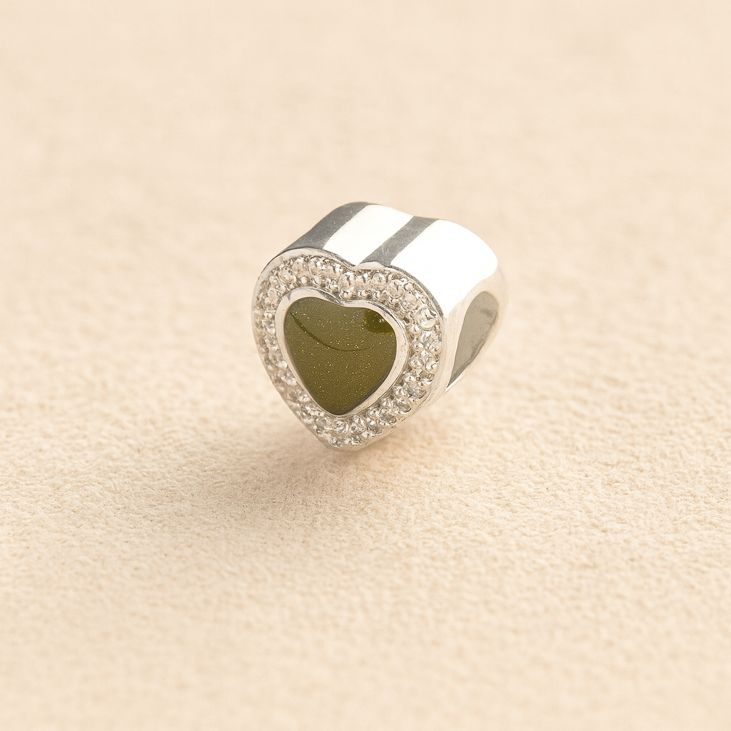 Heart-shaped silver ashes charm with a sage resin infill on a beige background